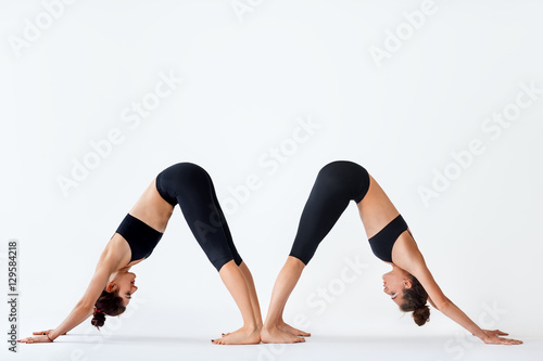 Two young women doing yoga asana Downward Facing Dog