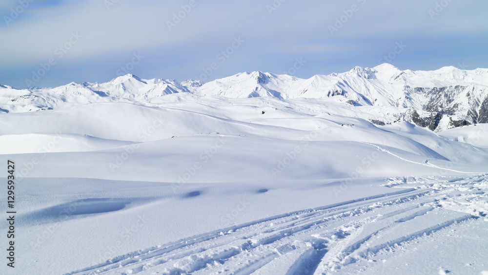 ski tracks on fresh snow in mountains with alpine peaks in the background