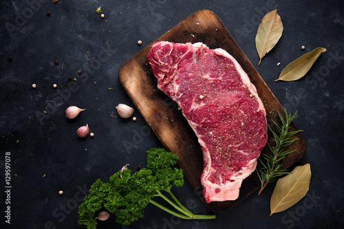 Papier peint Raw steak with rosemary, salt and pepper cooking over stone table background