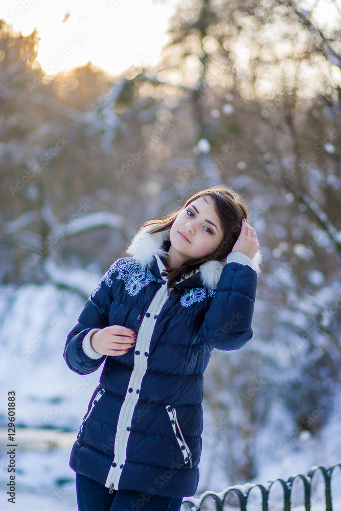 Beautiful girl in blue jacket standing in a snowy park near the Beautiful girl in blue jacket standing in a snowy park near the