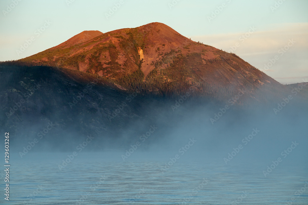 Fog over the lake and mountain peak in the red light. Lake Labynkyr. Yakutia. Russia.