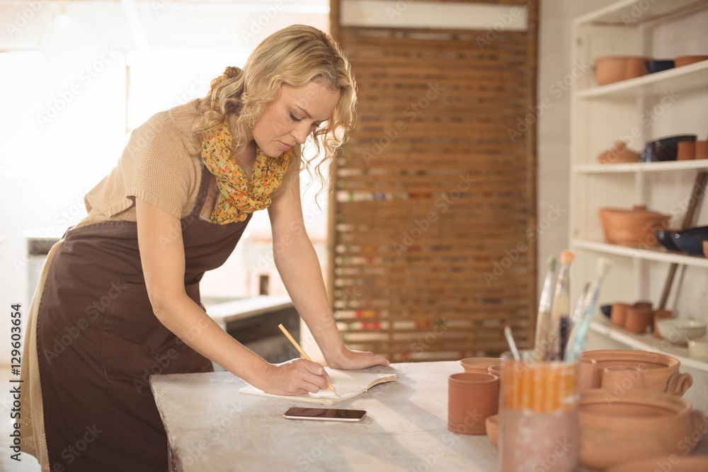 Female potter writing in notebook Female potter writing in notebook