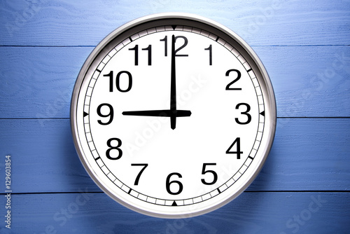 Round clock shows shows at 9 o'clock, clock on blue background