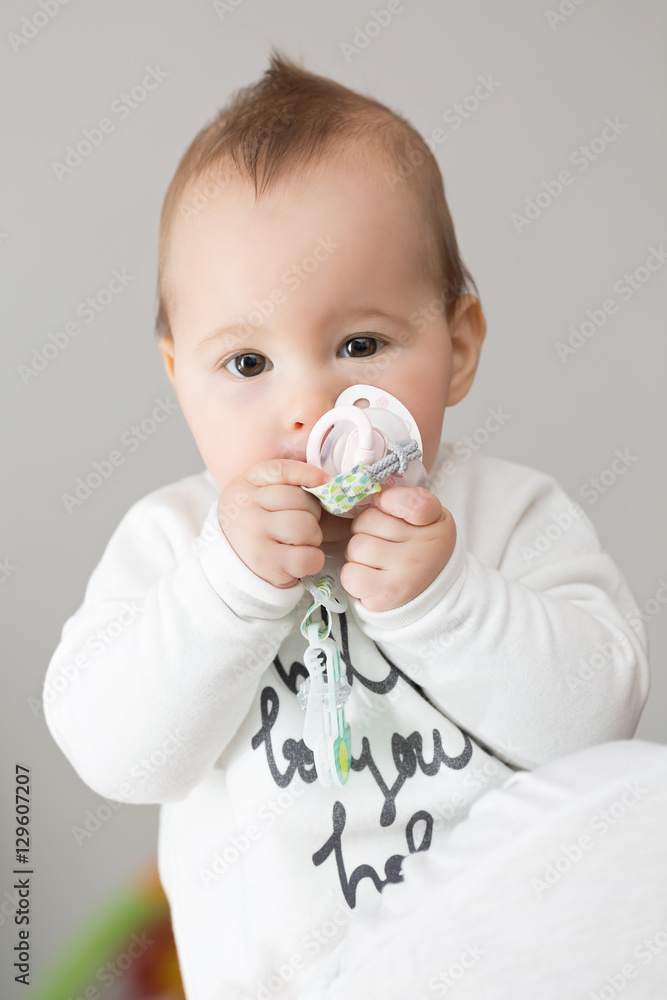 Eight months old baby girl bringing her pacifier to her mouth an