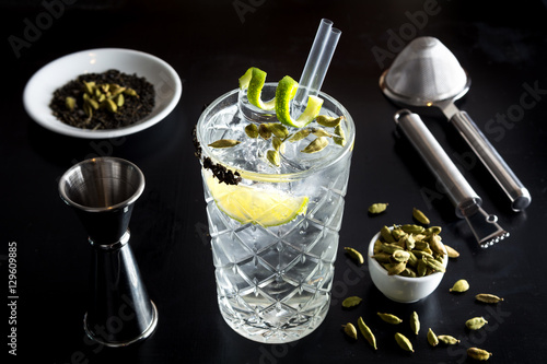 Obraz na płótnie Gin tonic drink cocktail fancy glass black background tonic water ice garnish fresh fruit craft cocktail cucumber orange peel decoration measure bottle lime peeler grapefruit w salonie