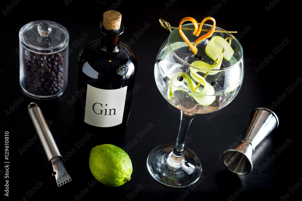 Gin tonic drink cocktail fancy glass black background tonic water ice garnish fresh fruit craft cocktail cucumber orange peel decoration measure bottle lime peeler grapefruit
