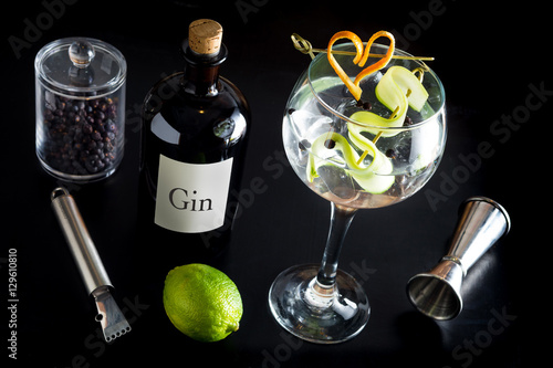 Obraz na płótnie Gin tonic drink cocktail fancy glass black background tonic water ice garnish fresh fruit craft cocktail cucumber orange peel decoration measure bottle lime peeler grapefruit w salonie