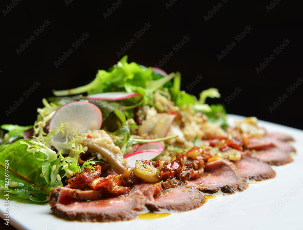 Sliced grilled beef steak with green leaves salad on rustic plat