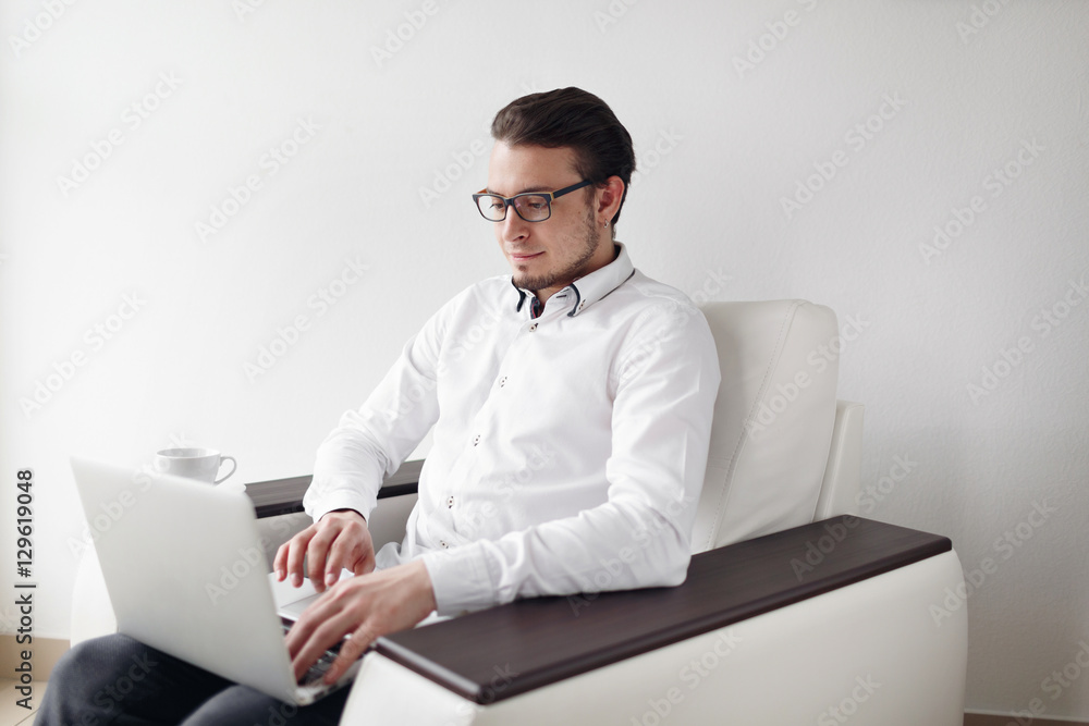 Young Man in Glasses checks mail sitting chair While Using Laptop. White Background. Young Man in Glasses checks mail sitting chair While Using Laptop. White Background.