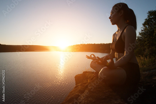 Young healthy woman is practicing yoga at mountain lake during s