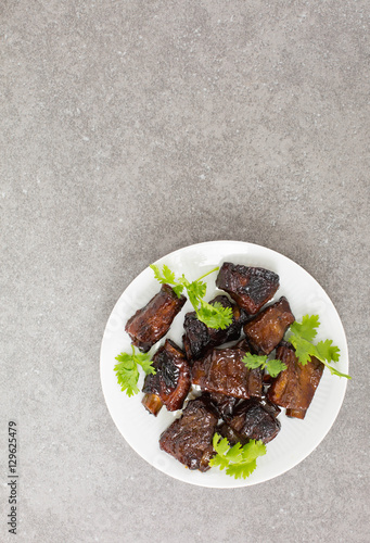 Chinese sweet and sour ribs. on a white plate. Dark gray stone background. Copy space. 