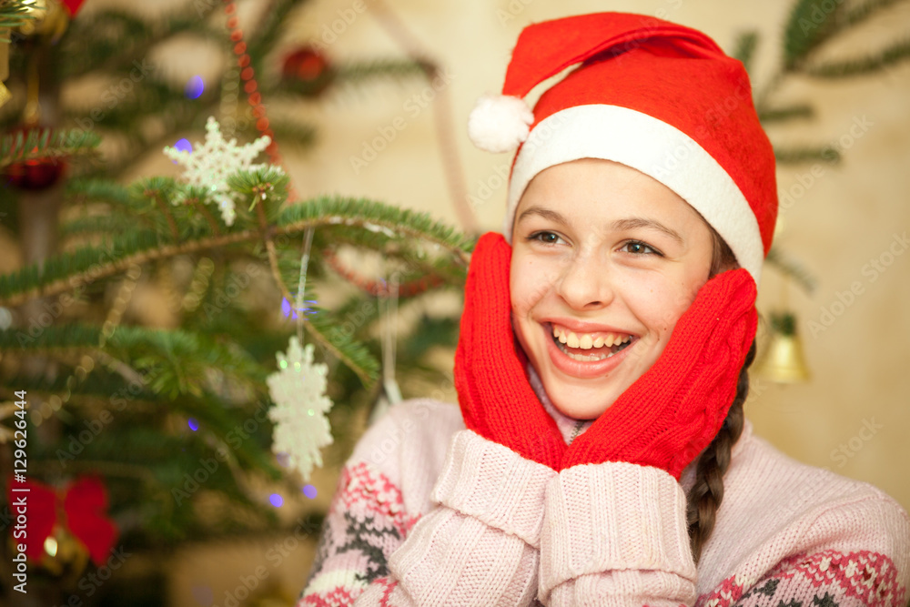Beautiful girl in santa hat near christmas tree