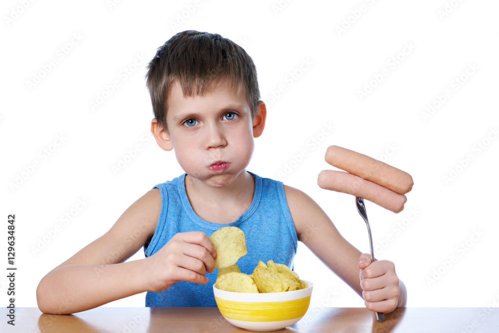 Little boy with fat cheeks eating sausages and potato chips isol Little boy with fat cheeks eating sausages and potato chips isol