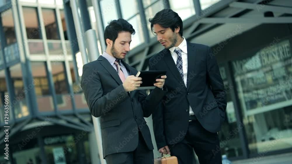 businessmen at work around financial building with tablet computer businessmen at work around financial building with tablet computer