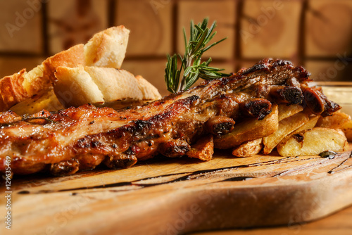 Pork ribs with potatoes and bread loafs on a wooden platter