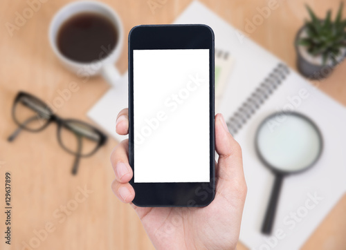 Business hand holding smart phone with white screen isolated on desk office background.