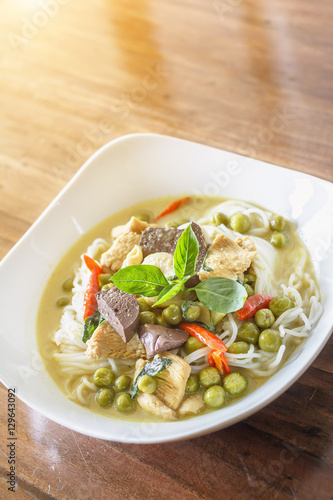 Green curry chicken with thai rice noodles in ceramic plate on wood table with sunlight background, Thai Food.