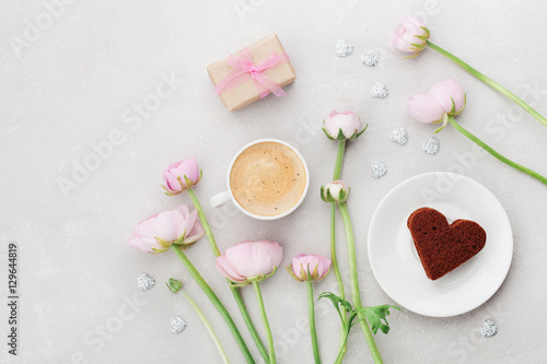 Breakfast for Valentines day with cup of coffee, gift, flowers and cake in shape of heart on gray table from above in flatlay style.