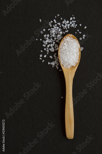 Spoon with white stone salt on black background © Svetlana