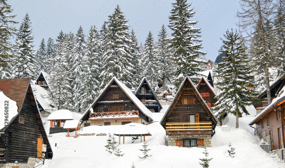 Winter idyll. Wooden houses covered with snow surrounded by pine trees