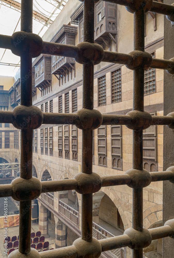 Cairo, Egypt - December 3 2016: View of the courtyard of caravansary (Wikala) of al-Ghuri through window with iron ornate grid, showing vaulted arcades and interleaved wooden grids (mashrabiya) Cairo, Egypt - December 3 2016: View of the courtyard of caravansary (Wikala) of al-Ghuri through window with iron ornate grid, showing vaulted arcades and interleaved wooden grids (mashrabiya)