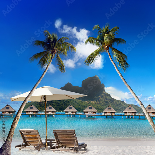 two beach chairs and solar umbrella under a palm tree and a view of the sea and mountains. Tahiti