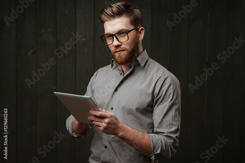 Man in eyeglasses holding tablet computer and looking away