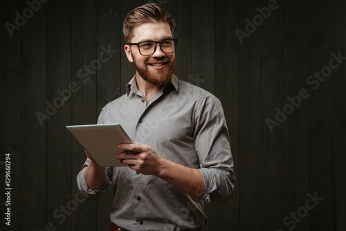 Man in eyeglasses holding tablet computer and looking away photo