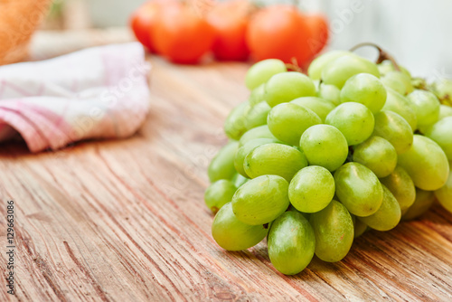 Grapes on wooden table, tomatoes in background - Text space on the left