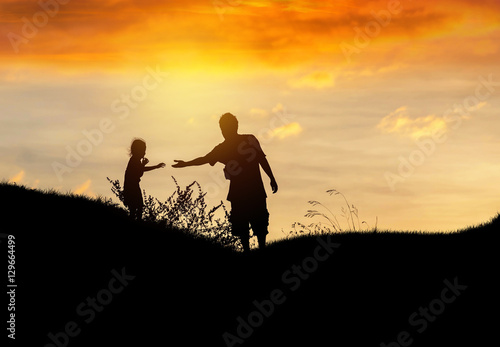 Silhouette father stretch hand helping to daughter on sunset © Soonthorn