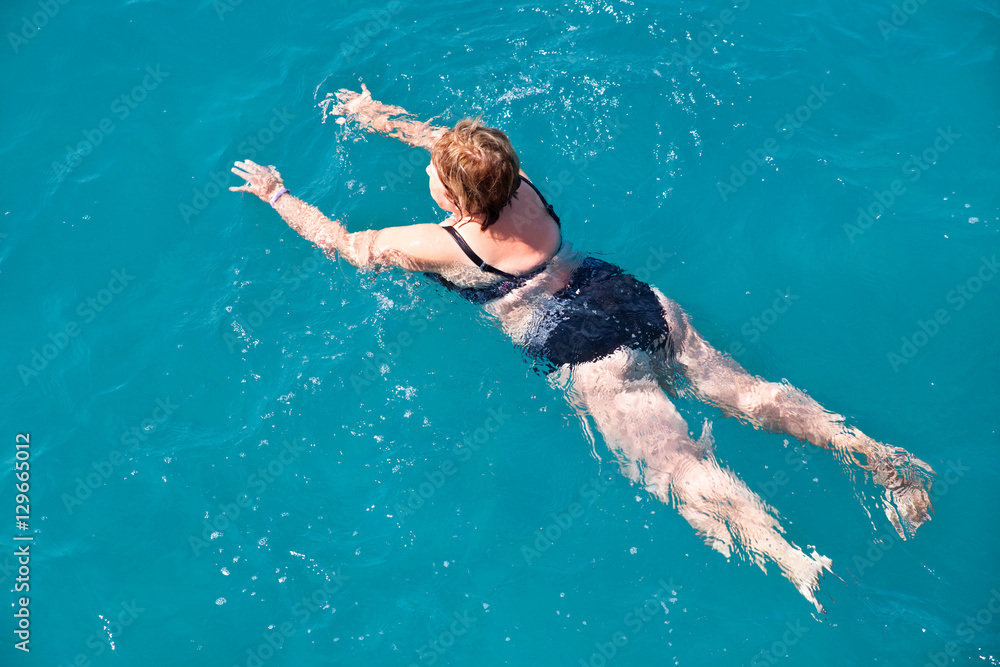 Active senior woman swimming in blue water