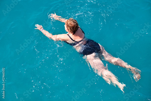 Active senior woman swimming in blue water