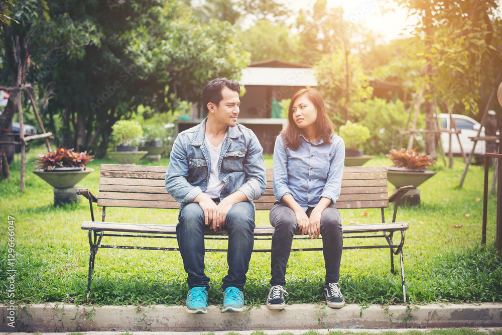 Young smiling couple looking on each other while sitting on benc Young smiling couple looking on each other while sitting on benc