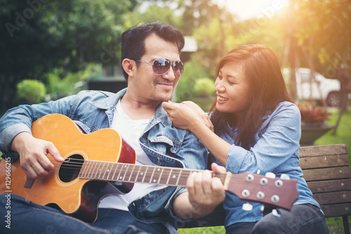Young couple in love playing acoustic guitar in the park while s © Johnstocker