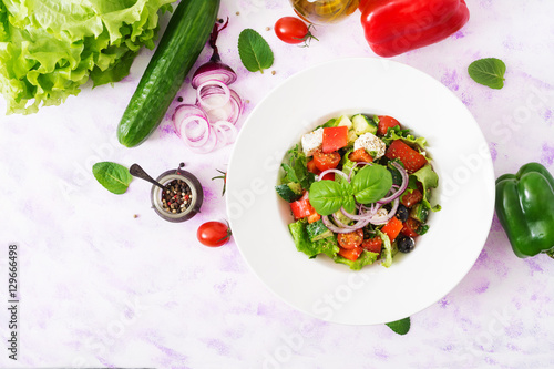 Greek salad with fresh tomato, cucumber, red onion, basil, lettuce, feta cheese, black olives and Italian herbs. Top view