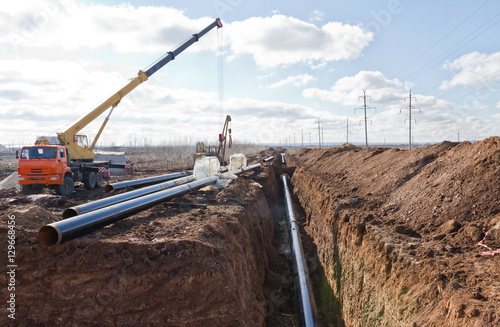 Construction work on the pipe laying of the pipeline into the trench using a crane