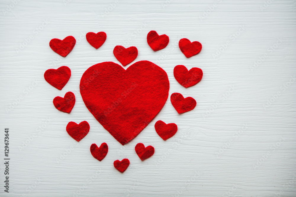 Красные сердца из фетра разного размера на белом деревянном столе.