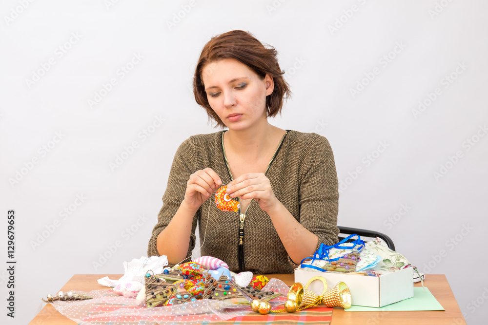 She sews toy cockerel at the table with needlework on a white background She sews toy cockerel at the table with needlework on a white background