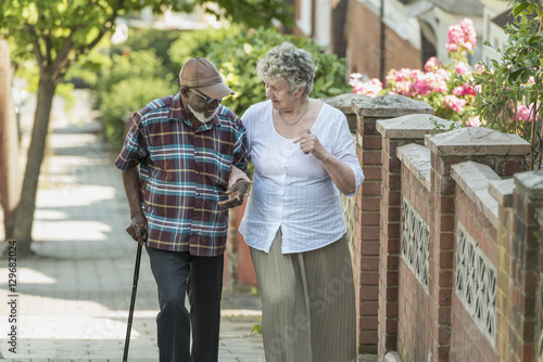 Tableau sur toile elderly inter racial couple help each other walk up a hill