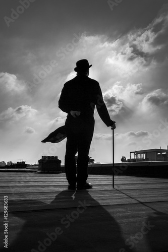 Black and white silhouette of a an elegant gentleman wearing a long a coattail with a cane and a  bowler hat