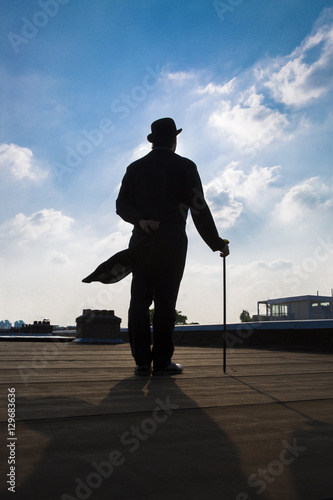 silhouette of a an elegant gentleman wearing a long a coattail with a cane and a  bowler hat
