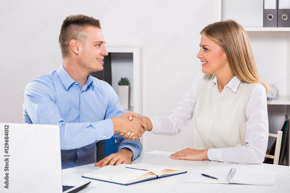 Businesswoman and businessman sitting in office and shaking hands.
Businesswoman and businessman sitting in office and shaking hands.