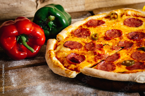Whole pizza with sausages and pepper on wood table with ingredients