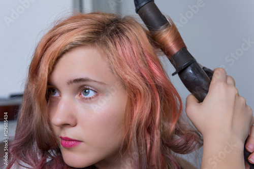 Closeup portrait of young woman using curling iron on hair