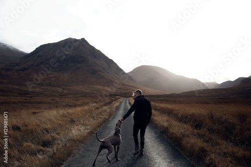 Man with dog walking on road against mountain photo