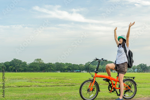 Young woman with backpack standing with bicycle in park, travel