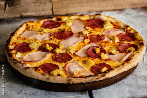 Pizza with ham, sausages and chicken on wood background