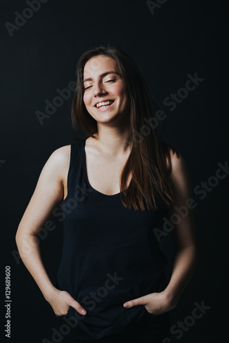Studio shot of young beautiful woman in black top smiling and posing isolated on black background. 