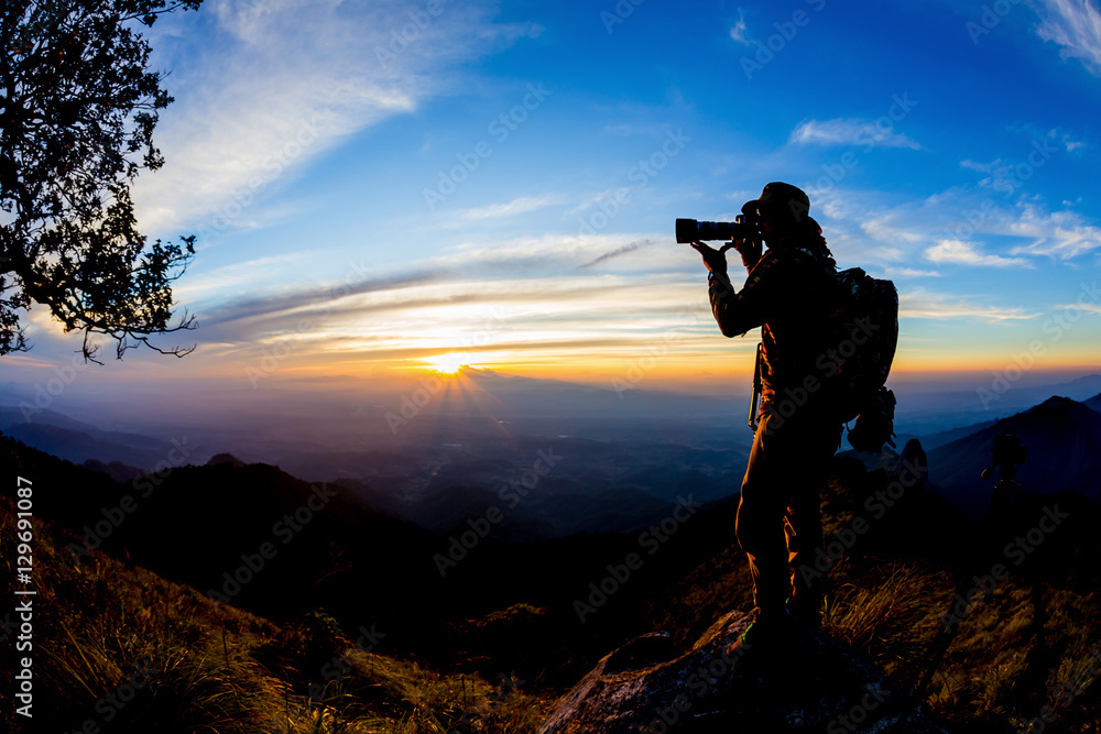 Silhouette of Young man with backpack taking a photo on the top Silhouette of Young man with backpack taking a photo on the top