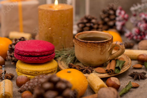 Cup of coffee, macaroons, cookies, walnuts, hazelnuts, cinnamon sticks, star anise, cone, candle, fir branch on sackcloth fabric